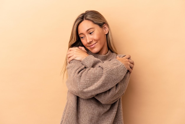 Jovem mulher caucasiana isolada em um fundo bege abraços, sorrindo despreocupada e feliz.