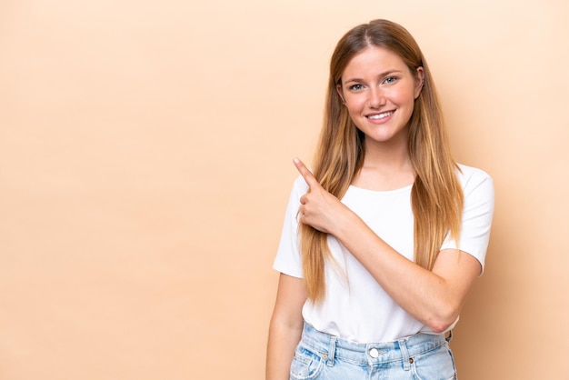 Jovem mulher caucasiana isolada em um fundo bege apontando para o lado para apresentar um produto