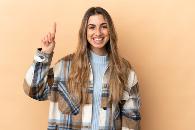 Jovem mulher caucasiana isolada em um fundo bege apontando para uma ótima ideia