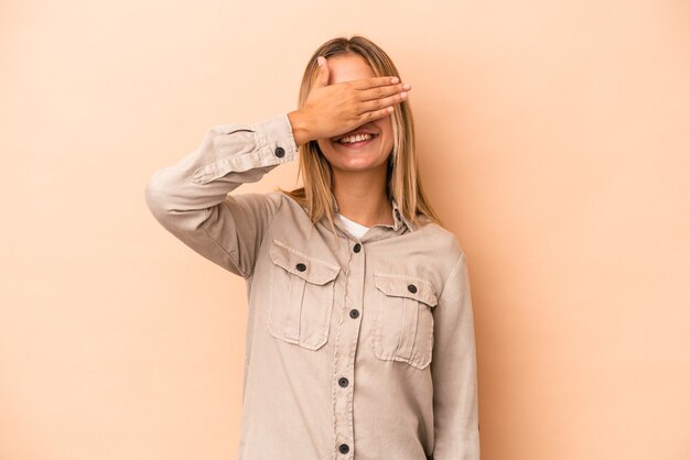 Foto jovem mulher caucasiana isolada em um fundo bege cobre os olhos com as mãos, sorri amplamente esperando por uma surpresa.