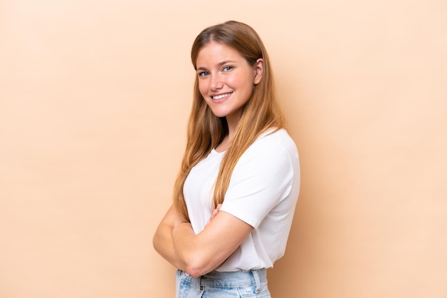 Jovem mulher caucasiana isolada em um fundo bege com os braços cruzados e olhando para a frente