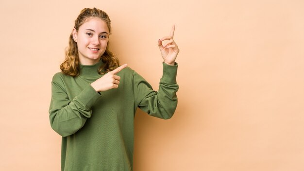 Jovem mulher caucasiana isolada em um fundo bege, dançando e se divertindo.