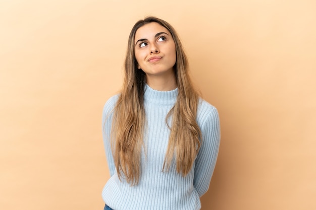 Foto jovem mulher caucasiana isolada em um fundo bege e olhando para cima