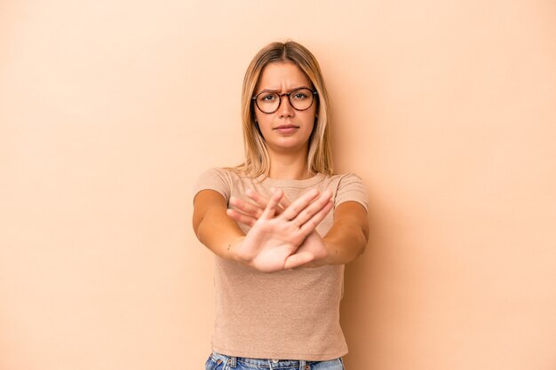 Jovem mulher caucasiana isolada em um fundo bege em pé com a mão estendida, mostrando o sinal de stop, impedindo você.