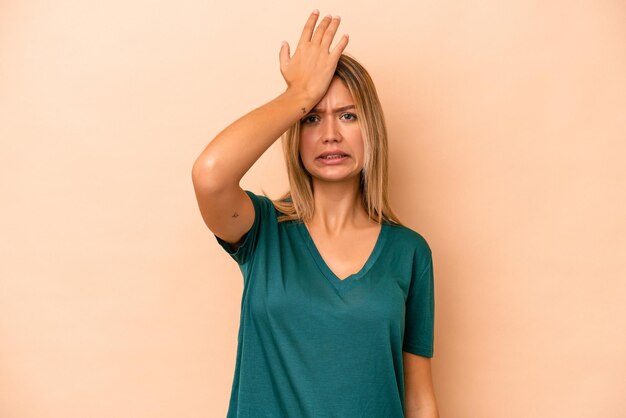 Jovem mulher caucasiana isolada em um fundo bege, esquecendo de algo, batendo na testa com a palma da mão e fechando os olhos.