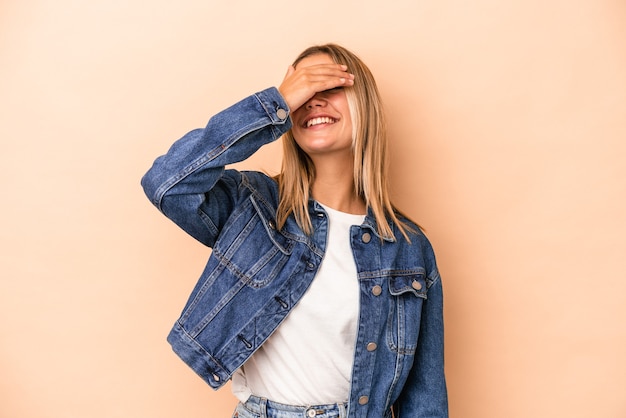 Jovem mulher caucasiana isolada em um fundo bege ri com alegria, mantendo as mãos na cabeça. Conceito de felicidade.