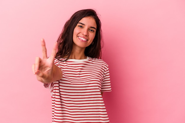 Jovem mulher caucasiana isolada em um fundo rosa alegre e despreocupada, mostrando um símbolo de paz com os dedos.