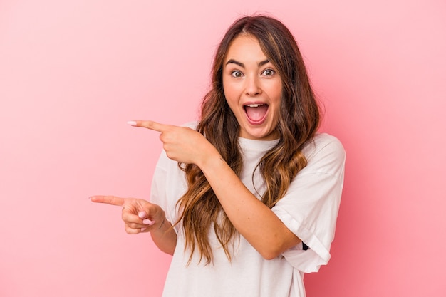 Jovem mulher caucasiana isolada em um fundo rosa animado apontando com os indicadores de distância.