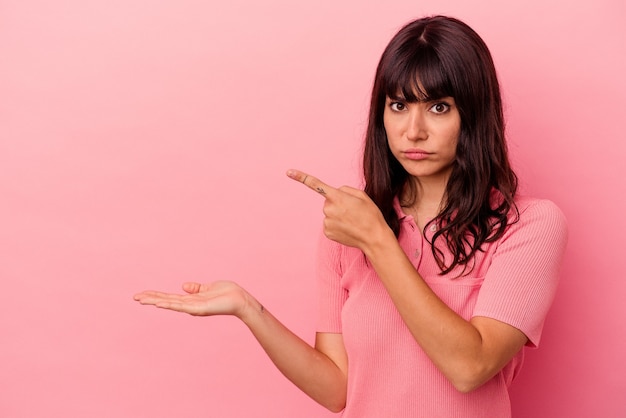 Jovem mulher caucasiana isolada em um fundo rosa animado segurando um na palma da mão.