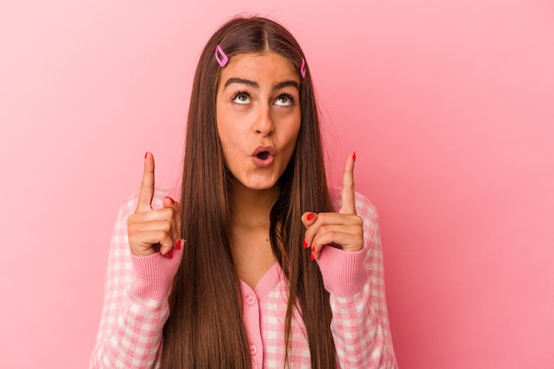 Jovem mulher caucasiana isolada em um fundo rosa apontando para cima com a boca aberta.