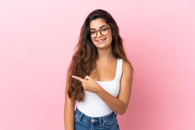 Jovem mulher caucasiana isolada em um fundo rosa apontando para o lado para apresentar um produto