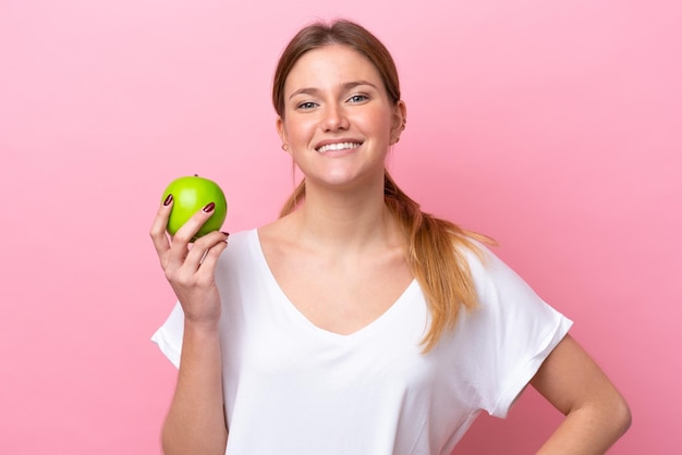 Jovem mulher caucasiana isolada em um fundo rosa com uma maçã e feliz