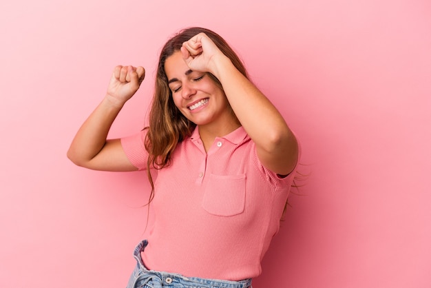 Jovem mulher caucasiana isolada em um fundo rosa, comemorando um dia especial, pula e levanta os braços com energia.