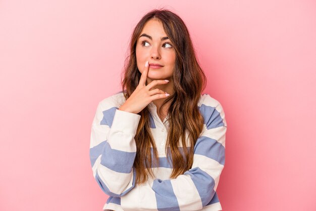 Jovem mulher caucasiana isolada em um fundo rosa, contemplando, planejando uma estratégia, pensando na forma de um negócio.