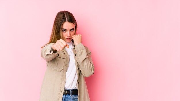 Jovem mulher caucasiana isolada em um fundo rosa dando um soco, raiva, lutando devido a uma discussão, boxe.