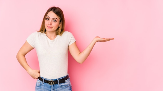 Jovem mulher caucasiana isolada em um fundo rosa duvidando e encolhendo os ombros os ombros em gesto de questionamento.