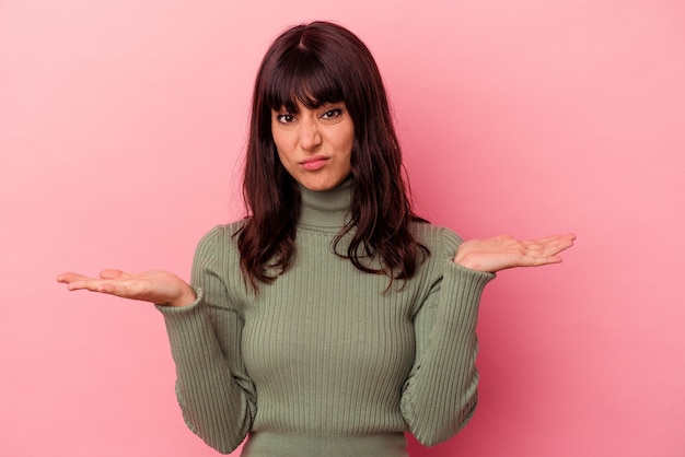 Jovem mulher caucasiana isolada em um fundo rosa duvidando e encolhendo os ombros os ombros em gesto de questionamento.