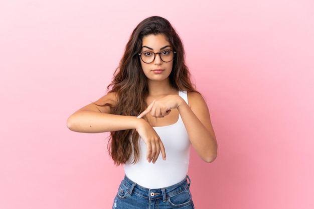 Jovem mulher caucasiana isolada em um fundo rosa fazendo o gesto de se atrasar