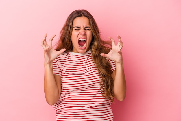 Jovem mulher caucasiana isolada em um fundo rosa, gritando de raiva.