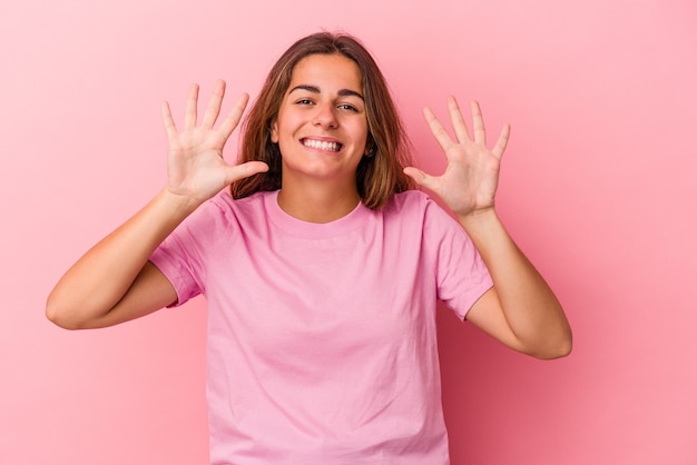 Jovem mulher caucasiana isolada em um fundo rosa, mostrando o número dez com as mãos.