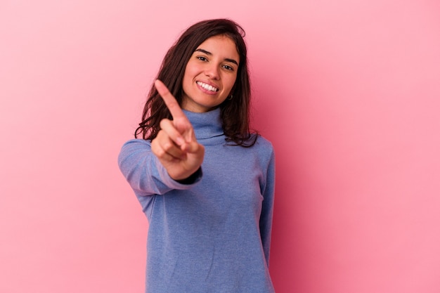 Jovem mulher caucasiana isolada em um fundo rosa, mostrando o número um com o dedo.