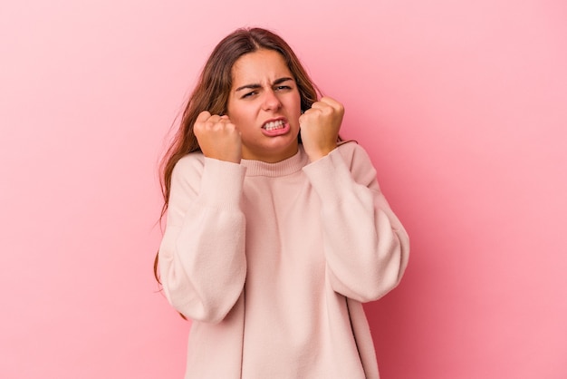 Jovem mulher caucasiana isolada em um fundo rosa, mostrando o punho para a câmera, expressão facial agressiva.