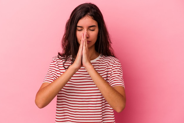 Jovem mulher caucasiana isolada em um fundo rosa orando, mostrando devoção, pessoa religiosa em busca de inspiração divina.