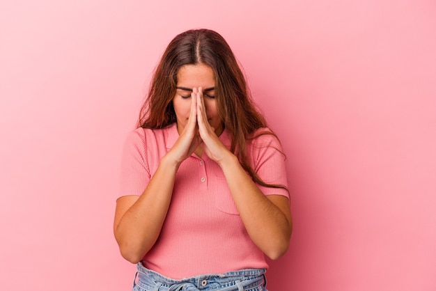 Jovem mulher caucasiana isolada em um fundo rosa orando, mostrando devoção, pessoa religiosa em busca de inspiração divina.