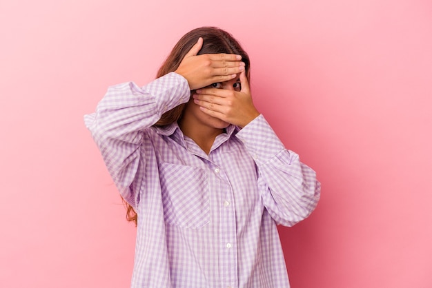 Foto jovem mulher caucasiana isolada em um fundo rosa piscar para a câmera por entre os dedos, o rosto coberto de vergonha.