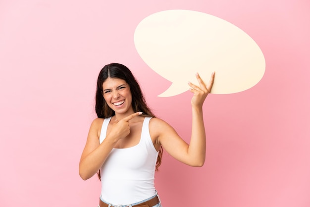 Jovem mulher caucasiana isolada em um fundo rosa segurando um balão de fala vazio e apontando-o