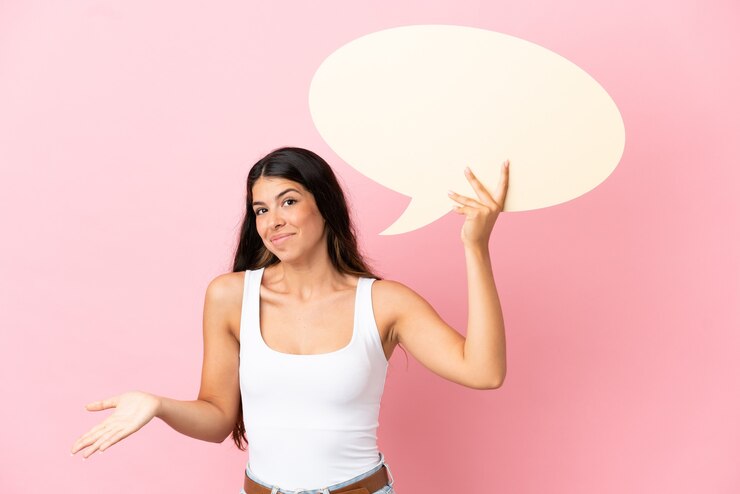 Foto jovem mulher caucasiana isolada em um fundo rosa segurando um balão de fala vazio e tendo dúvidas