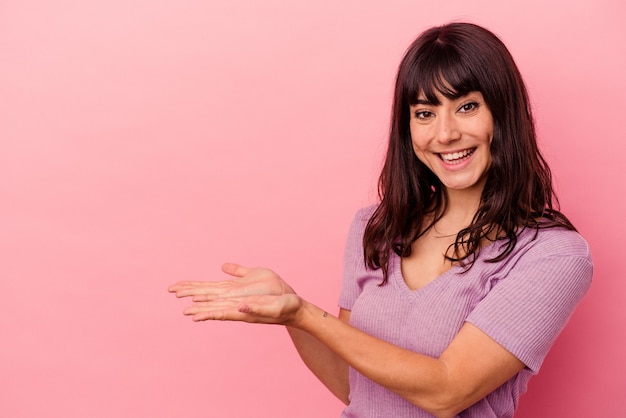 Jovem mulher caucasiana isolada em um fundo rosa, segurando um espaço de cópia na palma da mão.