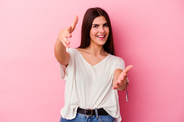 Jovem mulher caucasiana, isolada em um fundo rosa, sente-se confiante dando um abraço para a câmera.