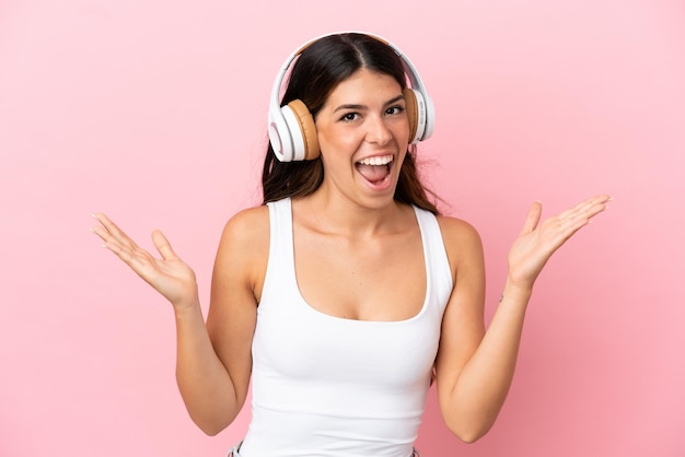 Jovem mulher caucasiana isolada em um fundo rosa surpresa e ouvindo música