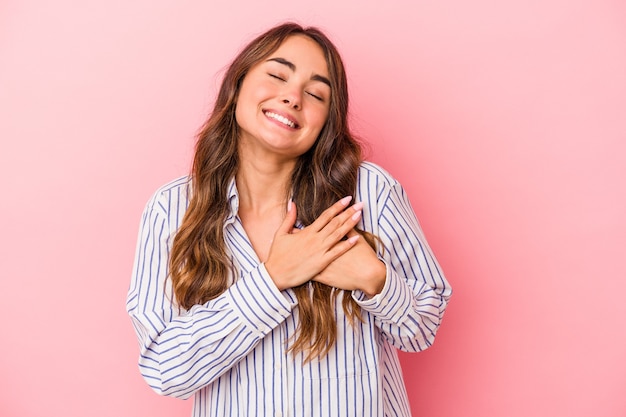 Jovem mulher caucasiana isolada em um fundo rosa tem uma expressão amigável, pressionando a palma da mão no peito. Conceito de amor.