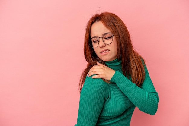 Jovem mulher caucasiana, isolada em um fundo rosa, tendo uma dor no ombro.