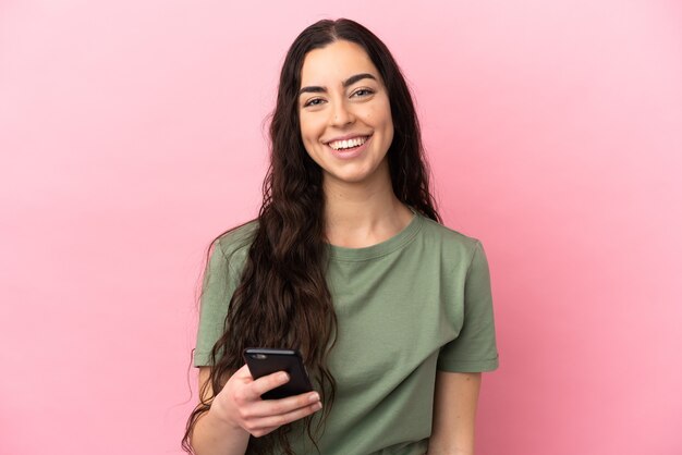 Jovem mulher caucasiana isolada em um fundo rosa usando telefone celular