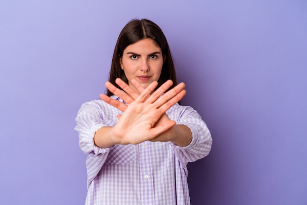 Jovem mulher caucasiana isolada em um fundo roxo fazendo um gesto de negação