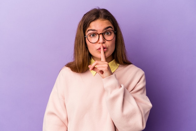 Jovem mulher caucasiana, isolada em um fundo roxo, mantendo um segredo ou pedindo silêncio.