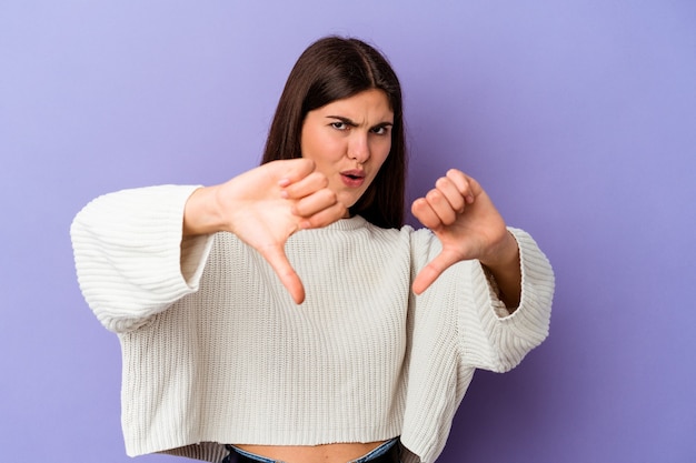 Jovem mulher caucasiana isolada em um fundo roxo, mostrando o polegar para baixo e expressando antipatia.