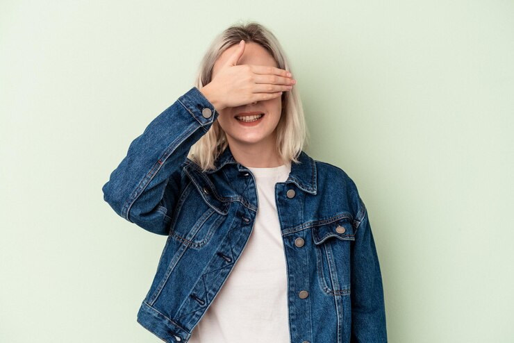 Foto jovem mulher caucasiana isolada em um fundo verde cobre os olhos com as mãos, sorrisos amplamente esperando por uma surpresa.