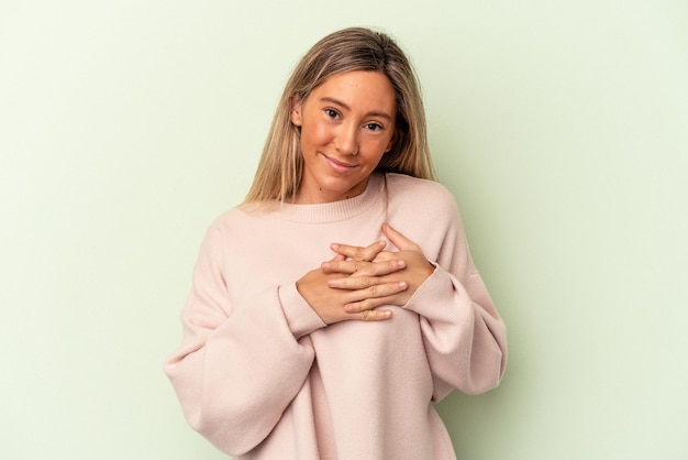 Jovem mulher caucasiana isolada em um fundo verde tem uma expressão amigável, pressionando a palma da mão no peito. conceito de amor.