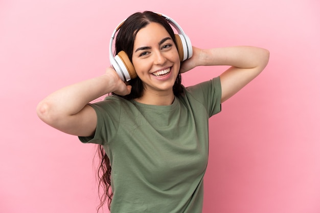 Jovem mulher caucasiana isolada em uma parede rosa ouvindo música