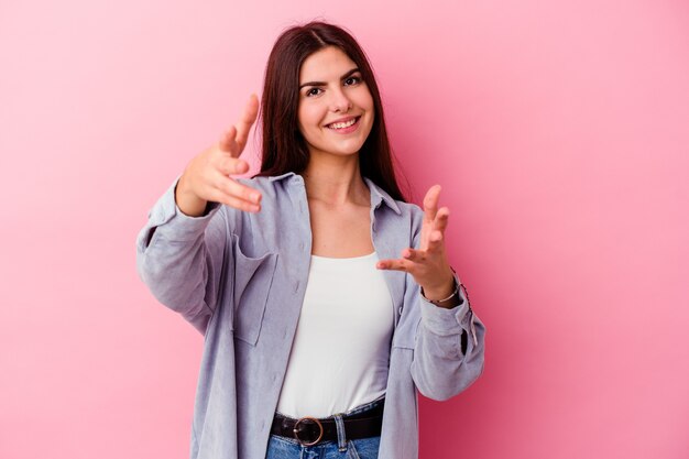 Jovem mulher caucasiana isolada em uma parede rosa se sente confiante para dar um abraço