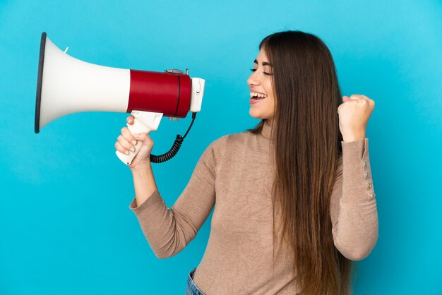 Jovem mulher caucasiana isolada gritando em um megafone para anunciar algo em posição lateral