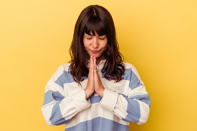 Jovem mulher caucasiana isolada na parede amarela orando, mostrando devoção, pessoa religiosa em busca de inspiração divina.