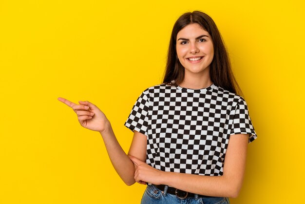 Jovem mulher caucasiana isolada na parede amarela sorrindo alegremente, apontando com o dedo indicador afastado.