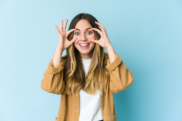 Jovem mulher caucasiana isolada na parede azul, mantendo os olhos abertos para encontrar uma oportunidade de sucesso.