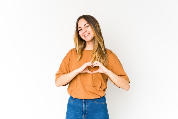 Foto jovem mulher caucasiana isolada na parede branca, sorrindo e mostrando uma forma de coração com as mãos.