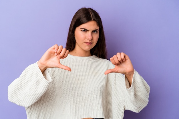 Jovem mulher caucasiana isolada na parede roxa, mostrando um gesto de antipatia, polegar para baixo